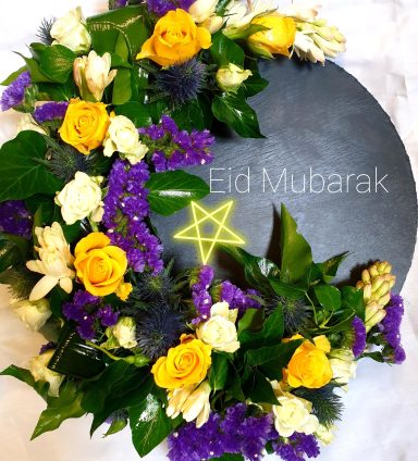 Floral wreath with yellow roses, purple flowers, and a star, featuring "Eid Mubarak" text.