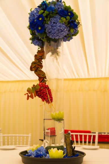 Tall floral arrangement with blue hydrangeas and decorative elements in a vase.