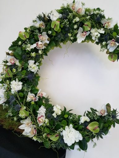 A circular floral wreath adorned with white and green flowers and foliage.
