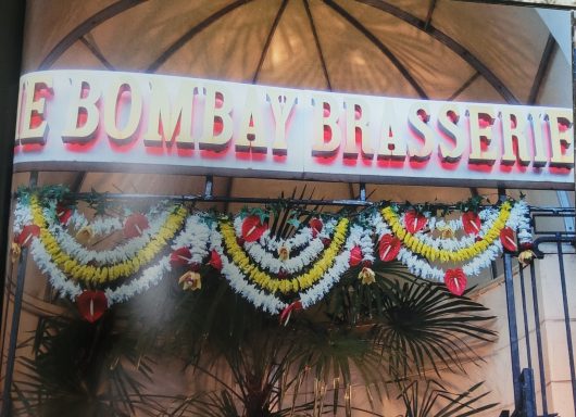 Sign for "The Bombay Brasserie" adorned with garlands and decorative elements.